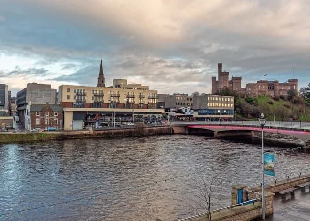 The River Ness in central Inverness with the Ness Bridge and Inverness Castle on its hill on the right, under a cloudy sky