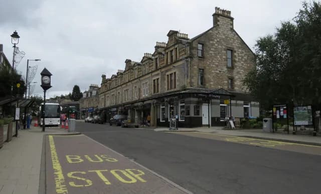 Atholl Road in Pitlochry: a stone terrace of shops along the main street, with a street clock and a bus stop