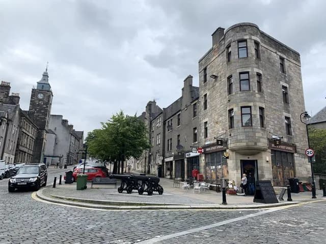 Cobbled Broad Street in Stirling's Old Town, with stone tenements, a pair of old cannon and a clock steeple at the far end