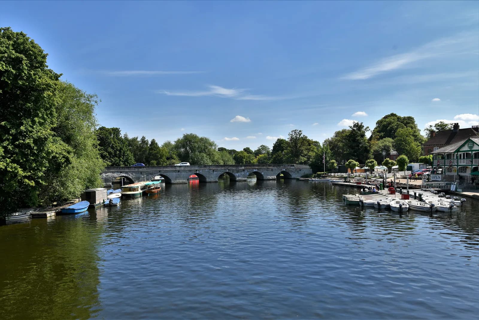 Clopton Bridge over the River Avon at Stratford-upon-Avon, with moored boats and the boathouse buildings at the right bank