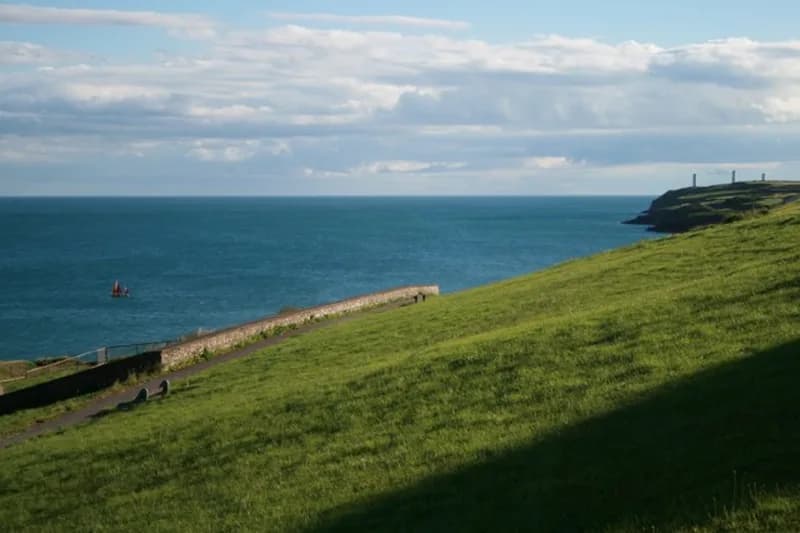 The grassy clifftop of the Doneraile Walk above Tramore Bay with the Great Newtown Head pillars beyond