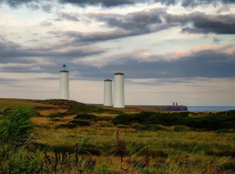 Three white beacon pillars on Great Newtown Head with the blue Metal Man figure on one of them