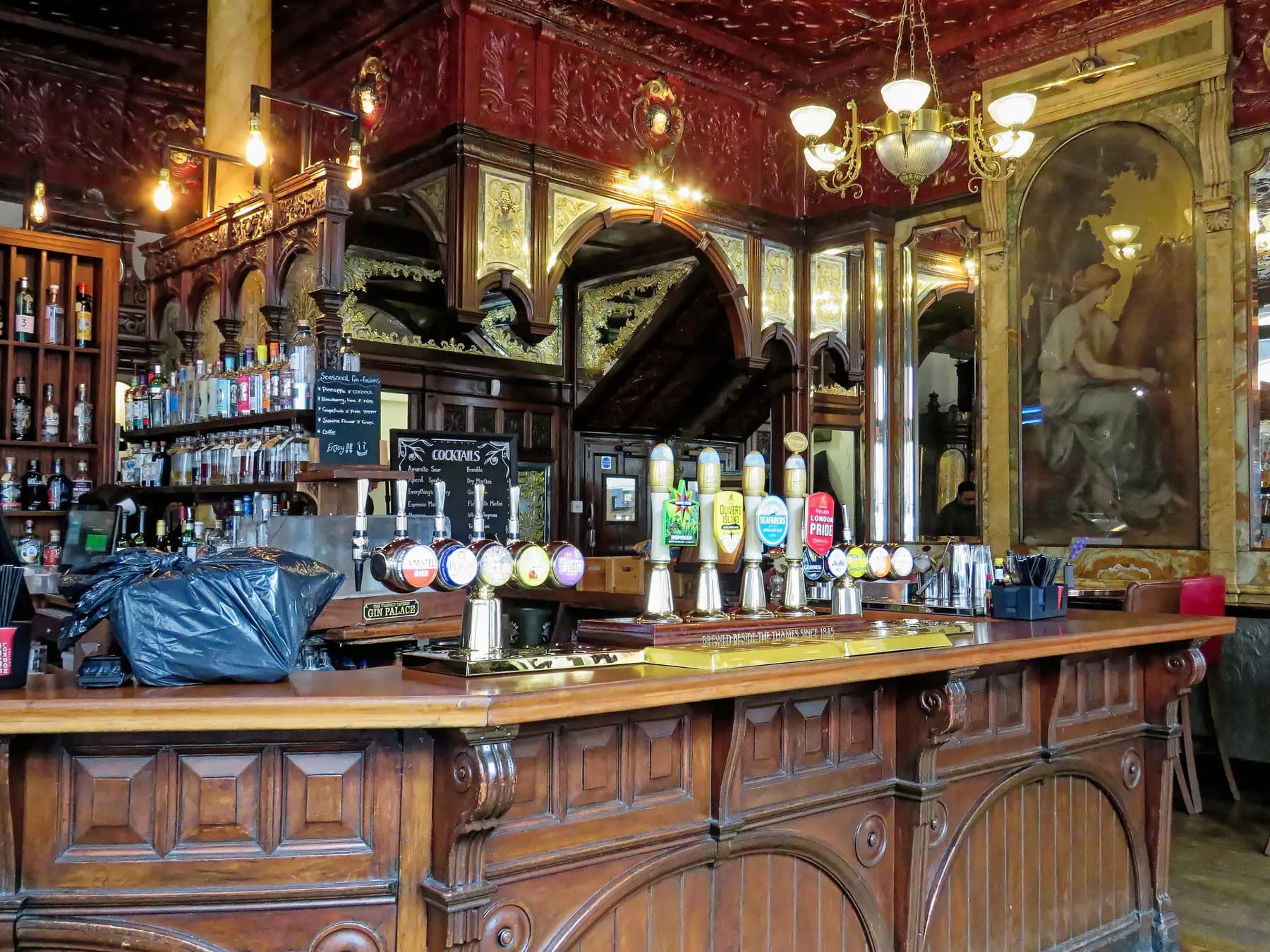 The ornate Victorian bar of the Viaduct Tavern on Newgate Street in London, with carved mahogany, etched mirrors, an embossed ceiling and a row of cask ale hand pumps